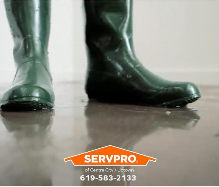 A person stands on a flooded floor in green rubber boots. 