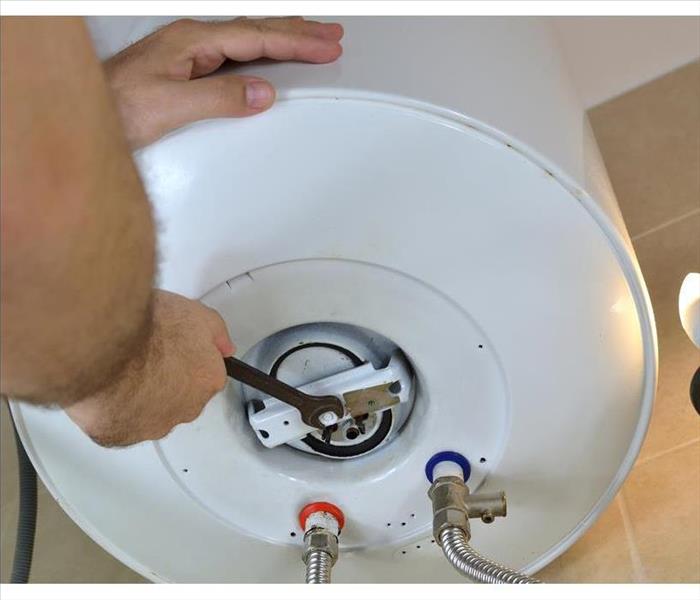 Man's hands unscrewing a screw-nut on a water heater with a wrench on a boiler in San Diego, CA